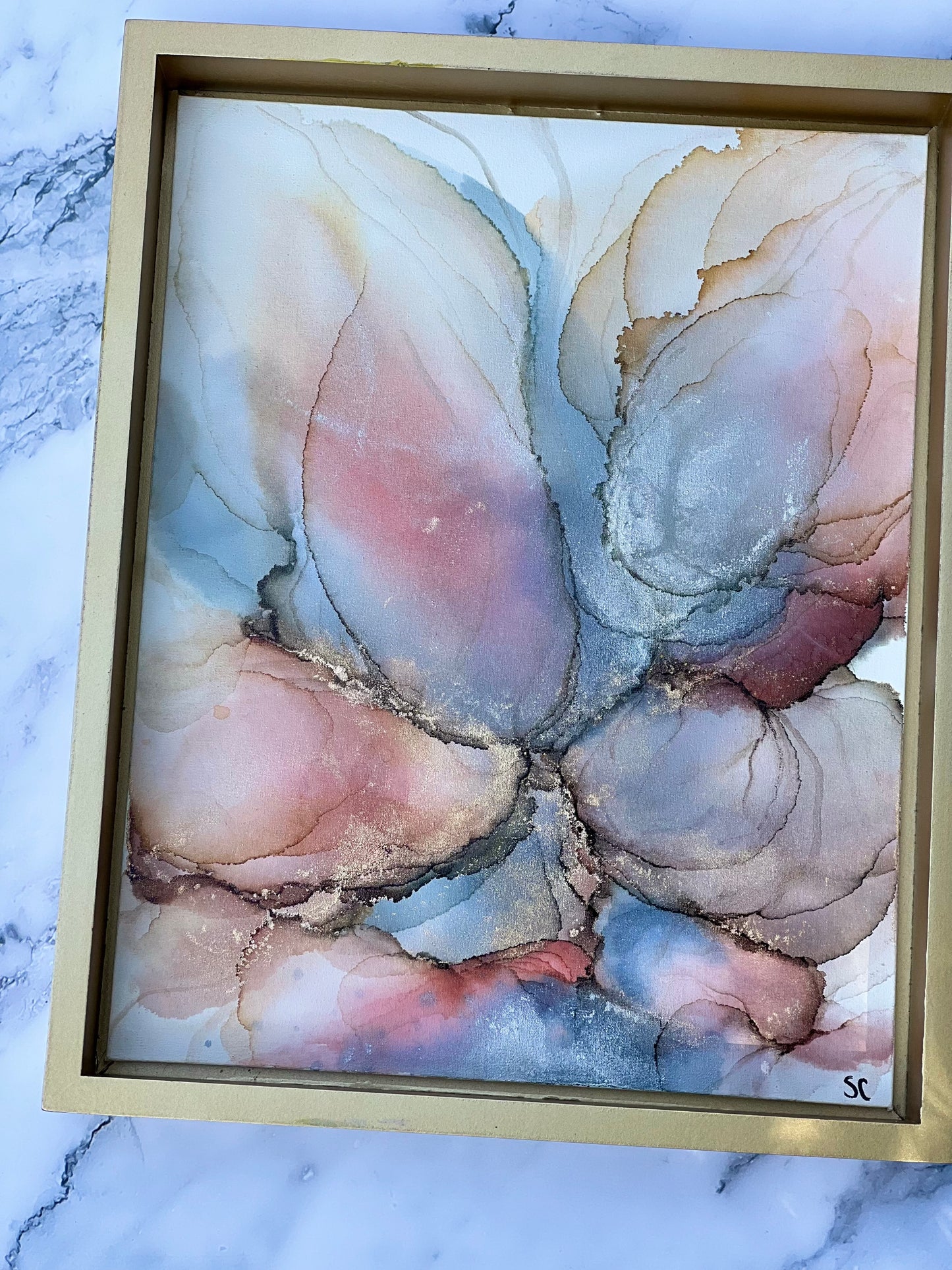 Original alcohol ink painting by Northeast Georgia artist Sarah Campbell, featuring abstract blush, gold, and blue petal-like forms with metallic accents in a gold frame.