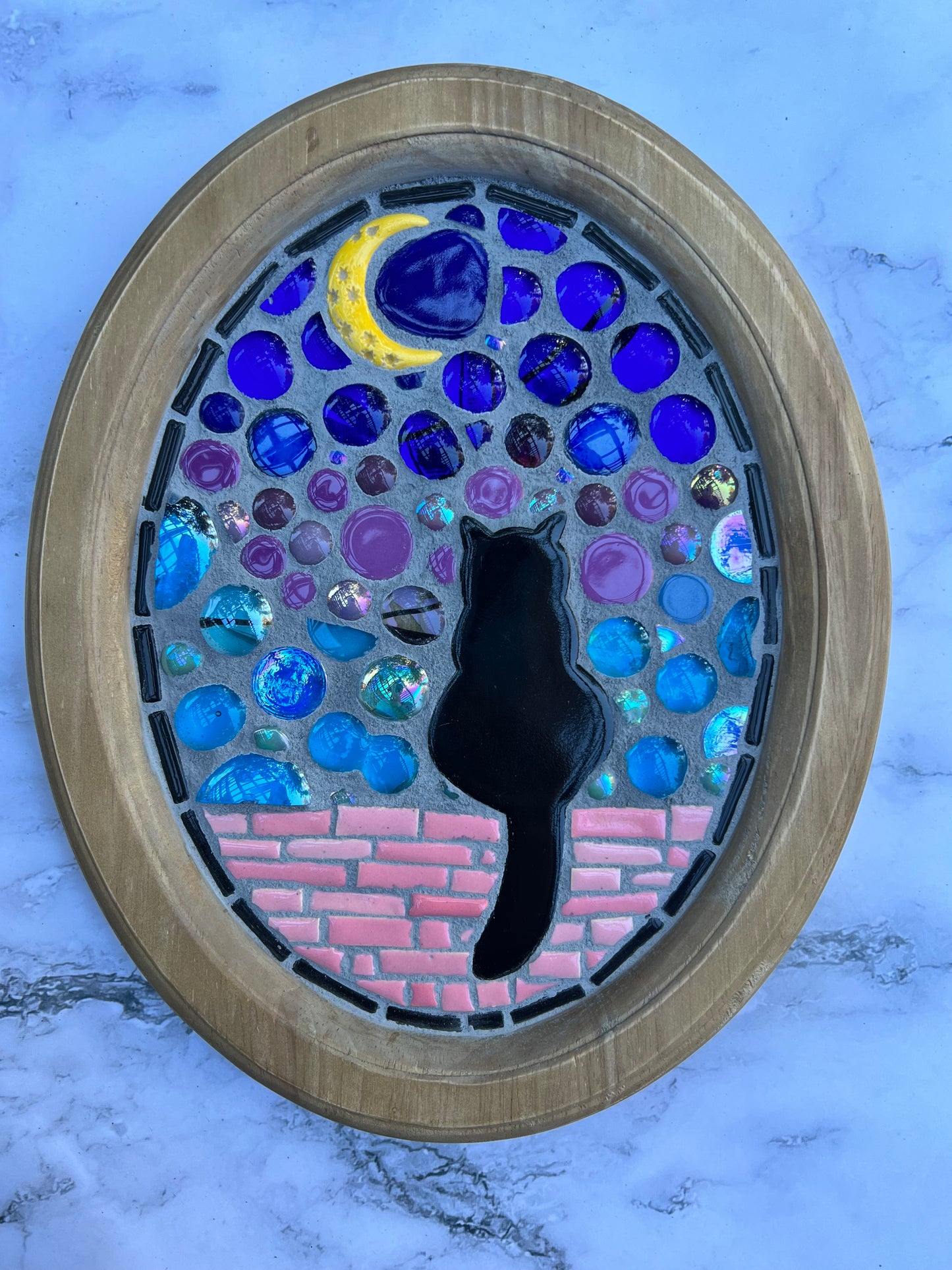 Handmade mosaic wall art by Northeast Georgia artist Sarah Campbell, featuring a black cat sitting on a pink brick wall under a crescent moon with stained glass and colorful gems in an oval frame.