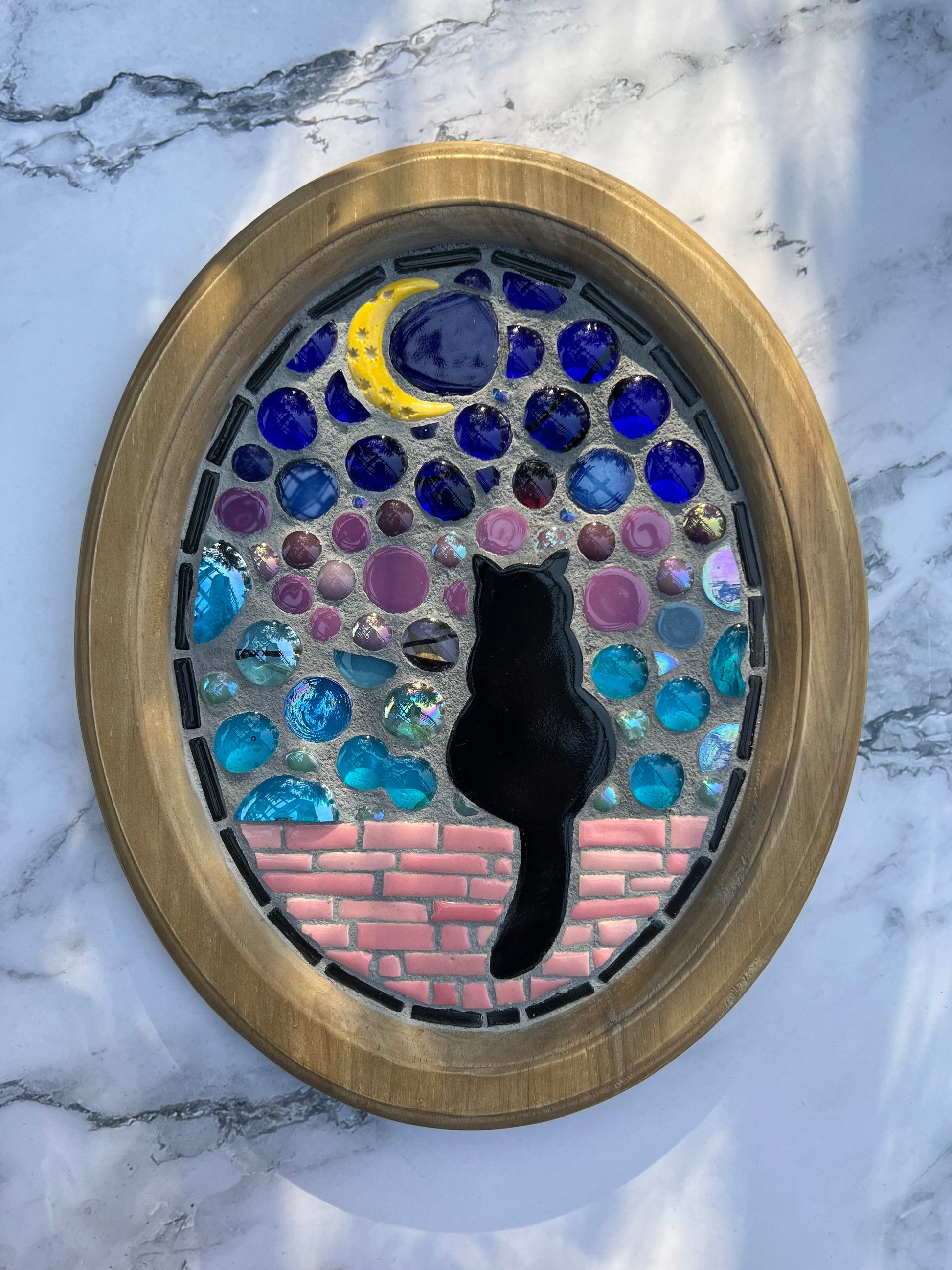 Handmade mosaic wall art by Northeast Georgia artist Sarah Campbell, featuring a black cat sitting on a pink brick wall under a crescent moon with stained glass and colorful gems in an oval frame.