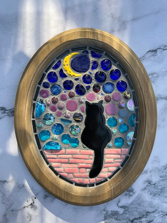 Handmade mosaic wall art by Northeast Georgia artist Sarah Campbell, featuring a black cat sitting on a pink brick wall under a crescent moon with stained glass and colorful gems in an oval frame.